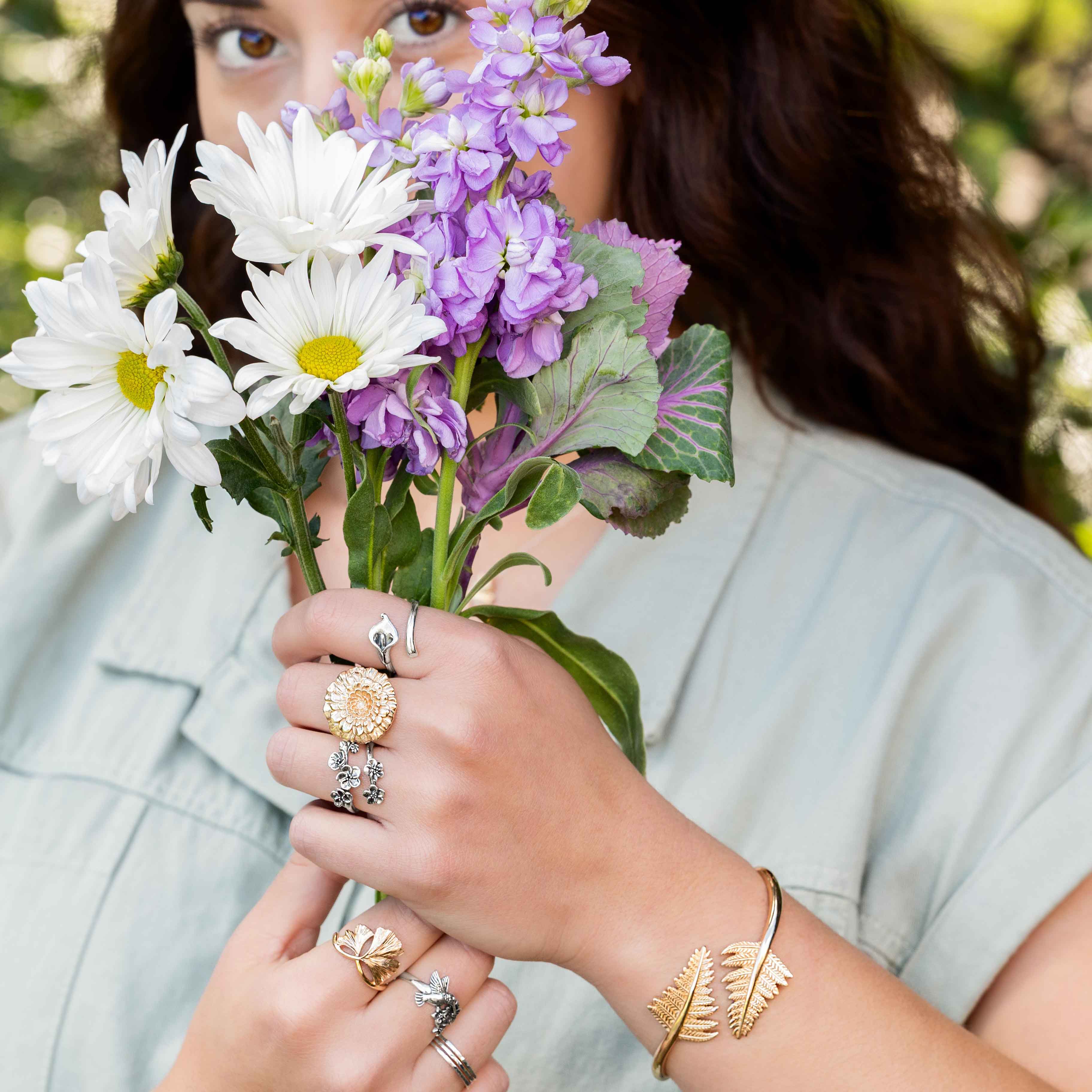 Woman with flowers in front of her face with rings on her hands