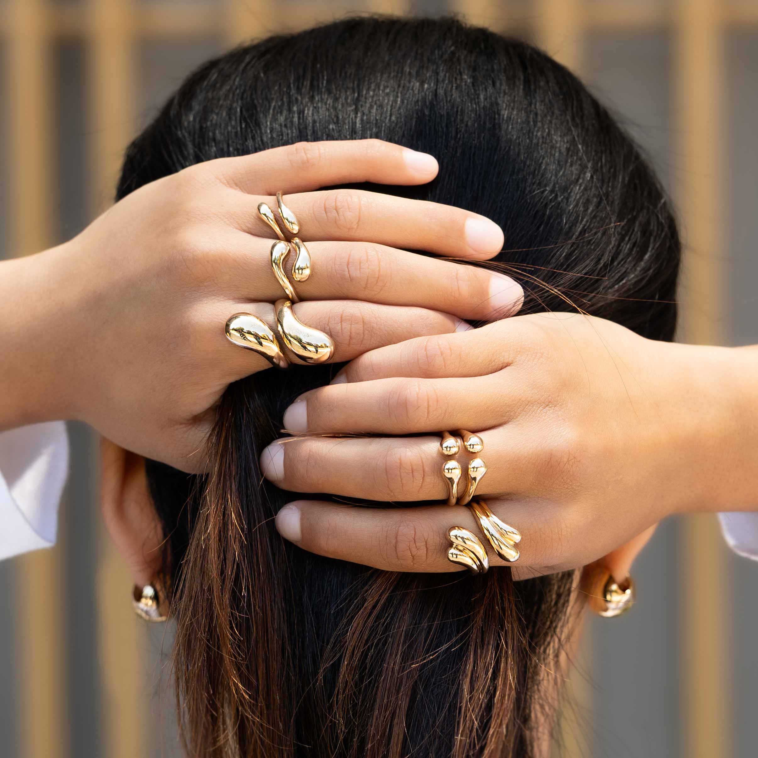 Woman wearing bronze rings with hands on head.