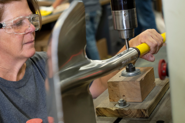 A close-up photo of a drill press drilling a hole into a shovel.