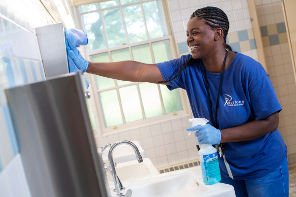A woman in a blue uniform wiping down a mirror.