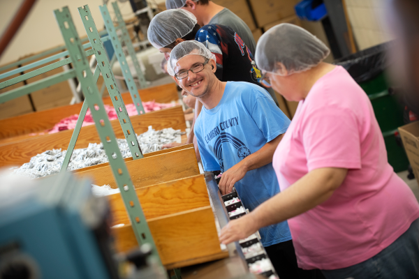 Two individuals in a warehouse. On a red background the words, “UniqueSource is one of the largest employers for people with disabilities in Pennsylvania.